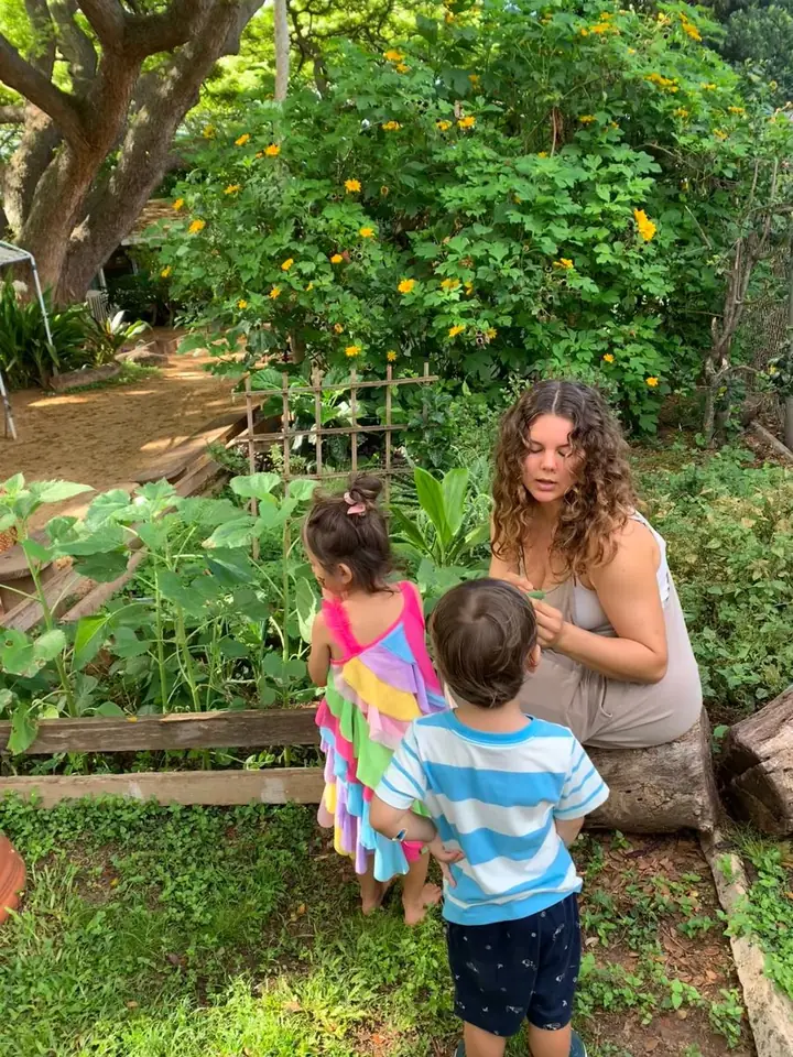 A Lumroot educator sitting in a garden, talking with two young children